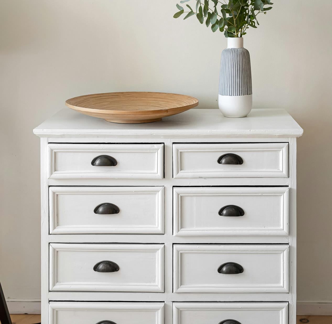 White painted chest of drawers with a wooden bowl and eucalyptus